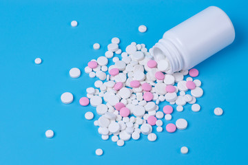 White and pink pills, tablets and white bottle on blue background.