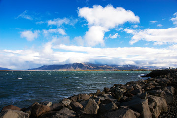 View of the Atlantic Ocean and the mountain covered with clouds from the embankment of Reykjavik on...
