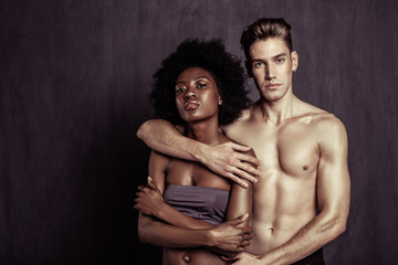 Beautiful multicultural couple standing together against grey background
