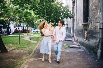 Fototapeta premium beautiful happy couple in love walking and gently hugging in sunny green street. stylish hipster groom and blonde bride embracing. romantic moments in summer city street on vacation
