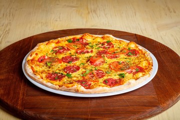 Pizza Italian pepperoni with melted cheese, salami, tomatoes and species on a white plate on a thick brown table