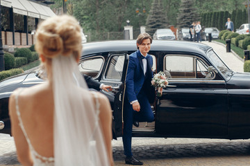 stylish bride looking at happy groom,  walking to her from car. luxury wedding couple first looks,...