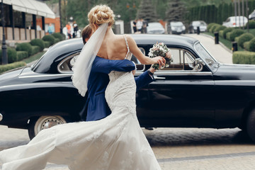 luxury wedding couple dancing at old car in light. stylish bride and groom hugging and embracing in...