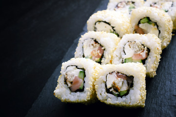 Sushi rolls sprinkled with sesame seeds. Ingredients: eel, salmon, cucumber, cream cheese, nori. Japanese rolls on a black plate.