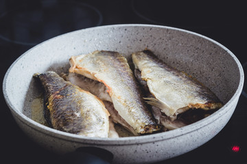 Fried sea bass fish with  golden crisp skin in a frying pan.