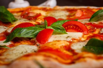 Close up Italian pizza margherita with melted mozzarella cheese, red cherry tomatoes and fresh green basil leaves on a brown table decorated by mushrooms, red sweet pepper and cherry tomatoes