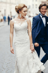 stylish bride walking and groom running after her in city street. happy luxury wedding couple having fun and dancing . romantic  moment.