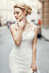 Fototapeta premium stylish bride posing on background of old wall in city street. luxury fashionable sexy woman in white dress walking in street