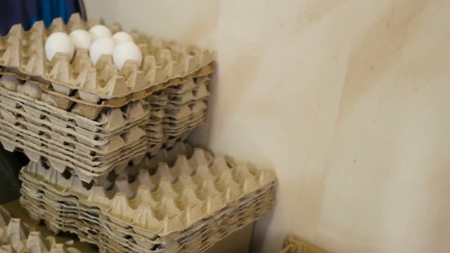 High stack of cardboard packaging from eggs near the wall. Side view, high angle, real time, smooth movement from bottom to top, natural light, indoors.