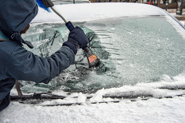 Man cleaning car windshield from ice with scraper tool.
