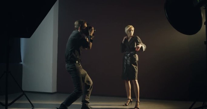 Caucasian young attractive female model posing in the dark studio space to the male professional photographer.