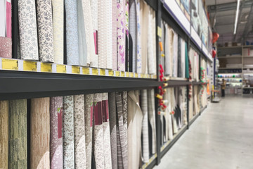 Shelves with a large selection of roll of wallpaper in the store. Colorful rolls of wallpaper as...