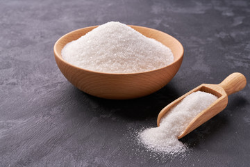 Wooden bowl and scoop with white sugar  on on a black background