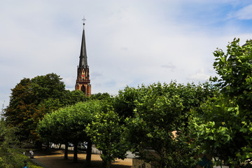 Historical church minaret between the trees near the river in Frankfurt am Main, Germany. City landscape photo with cloudy sky