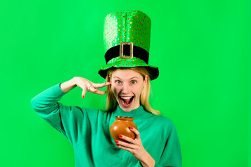Smiling blonde girl in Leprechaun costume holds pot with gold. Green hat. Leprechaun. Pot with...