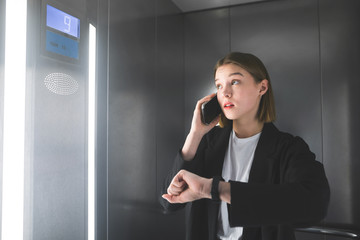 Young employee is looking at the floor number in the elevator talking by smartphone. Smart...