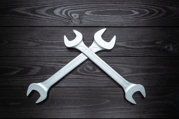 Crosshair of two chrome wrenches on dark wooden workbench.