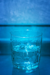 Hand made drinking glass filled with water against a blue background, half full. Conceptual serie: 2/3 (full, half full, empty).