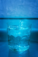 Hand made drinking glass filled with water against a blue background, full. Conceptual serie: 1/3 (full, half full, empty).