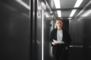 Thoughtful ambitious businesswoman is standing in the elevator and trying to remember somenthing. Puzzled female employee is thinking in the lift holding documents. © bodnarphoto