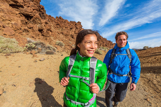 Happy Hikers On Mountain Climb Hike Trekking With Cold Jackets And Backpacks Healthy Active Lifestyle. Young Asian Woman With Caucasian Man Smiling Walking Outdoors.