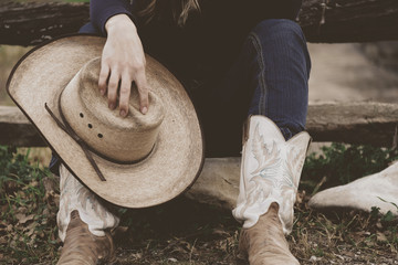 Girl holding cowboy hat while sitting with western boots on for agriculture industry lifestyle...