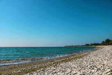 empty sea shore with white pebble, Landscape sand and round sones on the shore, trees far away, sea and blue sky. Travel. Unpopular place not for tourists. Cyprus, Mediterranian, Larnaca, Pervolia