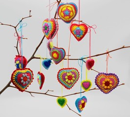 Fototapeta na wymiar Knitted hearts of colored yarn hang on a twig on a light background. Valentine's Day, love, handmade, amigurumi, hobby, decoration, postcard, creative.