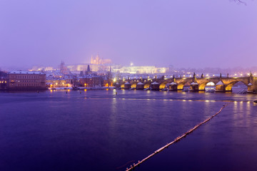 Obraz premium Foggy night Prague Lesser Town with gothic Castle, Bridge Tower and St. Nicholas' Cathedral in the Snowstorm, Czech republic