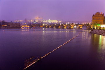 Obraz premium Foggy night Prague Lesser Town with gothic Castle, Bridge Tower and St. Nicholas' Cathedral in the Snowstorm, Czech republic