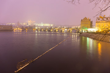 Obraz premium Foggy night Prague Lesser Town with gothic Castle, Bridge Tower and St. Nicholas' Cathedral in the Snowstorm, Czech republic