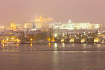 Fototapeta na wymiar Foggy night Prague Lesser Town with gothic Castle, Bridge Tower and St. Nicholas' Cathedral in the Snowstorm, Czech republic