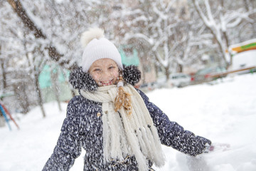 Child girl playing with folling snow in winter park