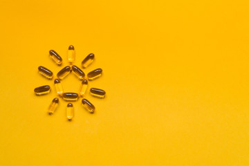 Close up capsules of fish fat oil in the sun shape, omega 3, vitamin e on the yellow background. Healthy food diet. Nutritional supplement