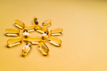 Close up capsules of fish fat oil in the sun shape, omega 3, vitamin e on the yellow background....