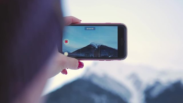 Young woman using her smart phone, taking pictures of winter nature in the mountains.