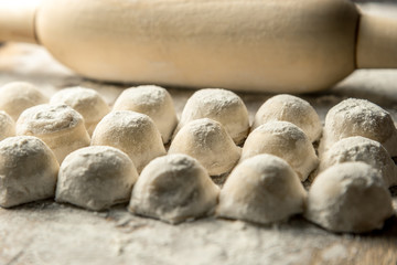 Fototapeta na wymiar Uzbek national food Chuchvara, like dumplings, with a rolling pin, on a wooden board, in flour