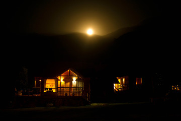 Fototapeta na wymiar night sunset in the mountains. the moon sets behind the mountains. foreground houses with lanterns