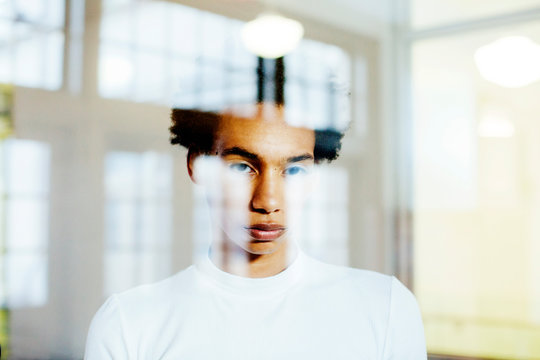 Portrait of a young man looking out the window with reflections of large windows shaping his face in the form of a cross