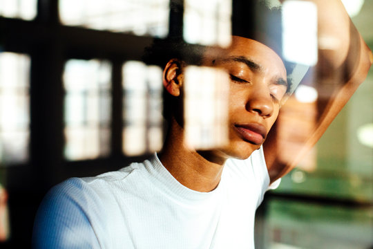 Portrait of a young man with eyes closed, standing against large windows