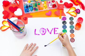 Child paints watercolors. Word love written on paper.