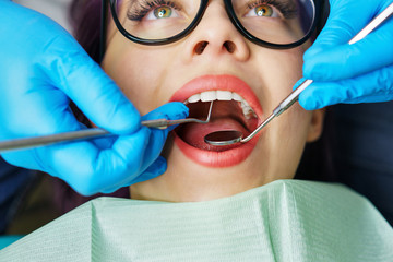 Routine examination at dentist. Young girl with open mouth. White teeth. Hands with medical instrument. Close-up.