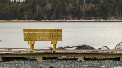 wooden bench on wooden boardwalk in winter, rocks, snow, water's edge.