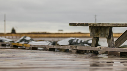 wooden bench on wooden boardwalk in winter, rocks, snow, water's edge.