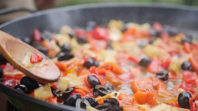 Closeup on the traditional way of cooking paella. Vegetarian one with olives, tomatoes, onions.