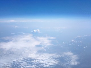 View from the high angle of the sky, clouds, fluffy, soft, space with shades of blue sky and earth background from above flying airplane window in bright morning sunrise 