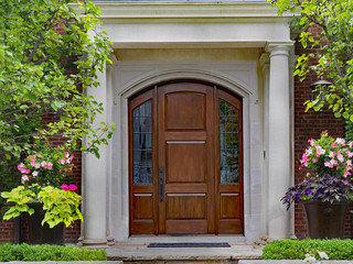 Fototapeta na wymiar elegant wooden front door and portico entrance surrounded by flowers of upper class house