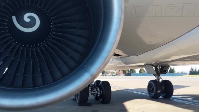 Widebody aircraft engine slowly turning in the wind, with landing gear in the background.