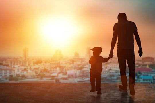 Child, baby holding an adult's hand. Father and son on a walk. Happy lovely baby on a wooden terrace with sun sets blurred. Little baby having fun time activity .silhouette concept.