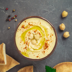 Chickpea hummus in a bowl, cheackpeas, pepper, parsley and pita bread on grey background. Top view, copy space.